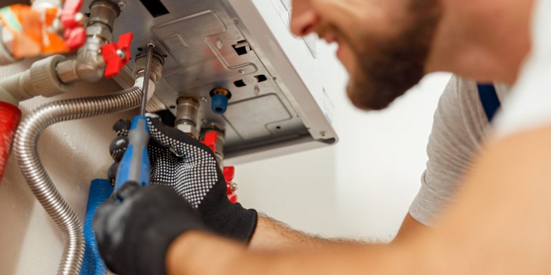 Closeup of plumber using screwdriver while installing new steel hot water central heating system in apartment. Manual work, maintenance, repair service concept