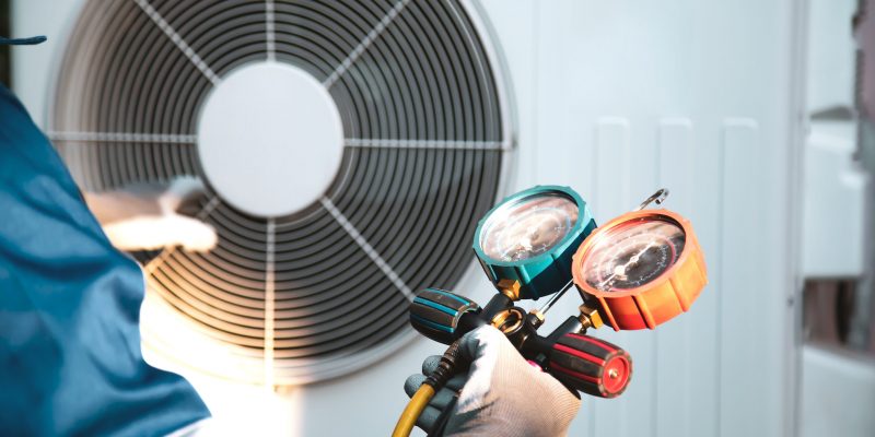 Mechanic air conditioner technician using manifold gauge checking refrigerant for filling home air conditioning and air duct cleaning and maintenance outdoor compressor unit.